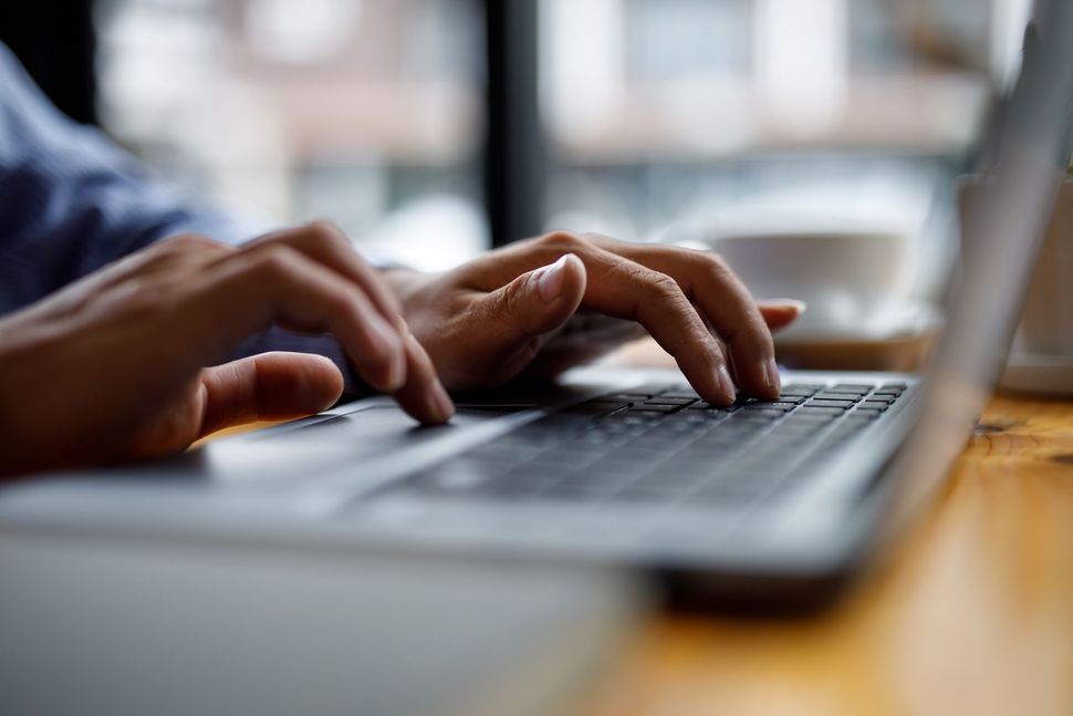 Hands typing on a laptop keyboard at a wooden table near a window. Hands typing on a laptop keyboard at a wooden table near a window.