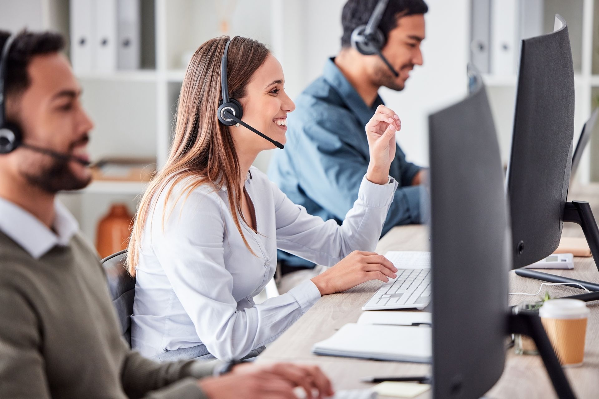 Customer service representatives at desks with headsets and computers, smiling.