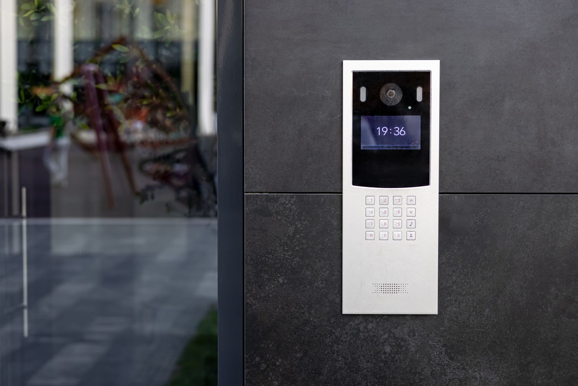 Silver intercom system mounted on a dark gray wall, displaying time. Silver intercom system mounted on a dark gray wall, displaying time.