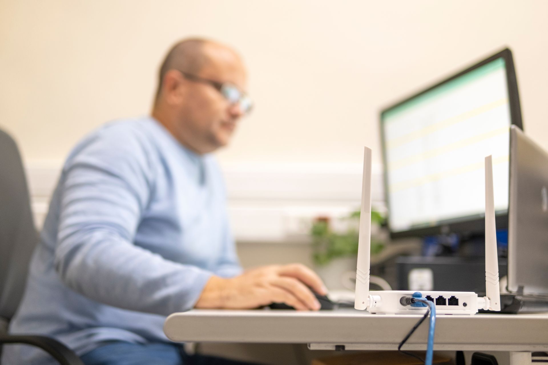 White wireless router with antennas in focus, blurred man using a computer in background.