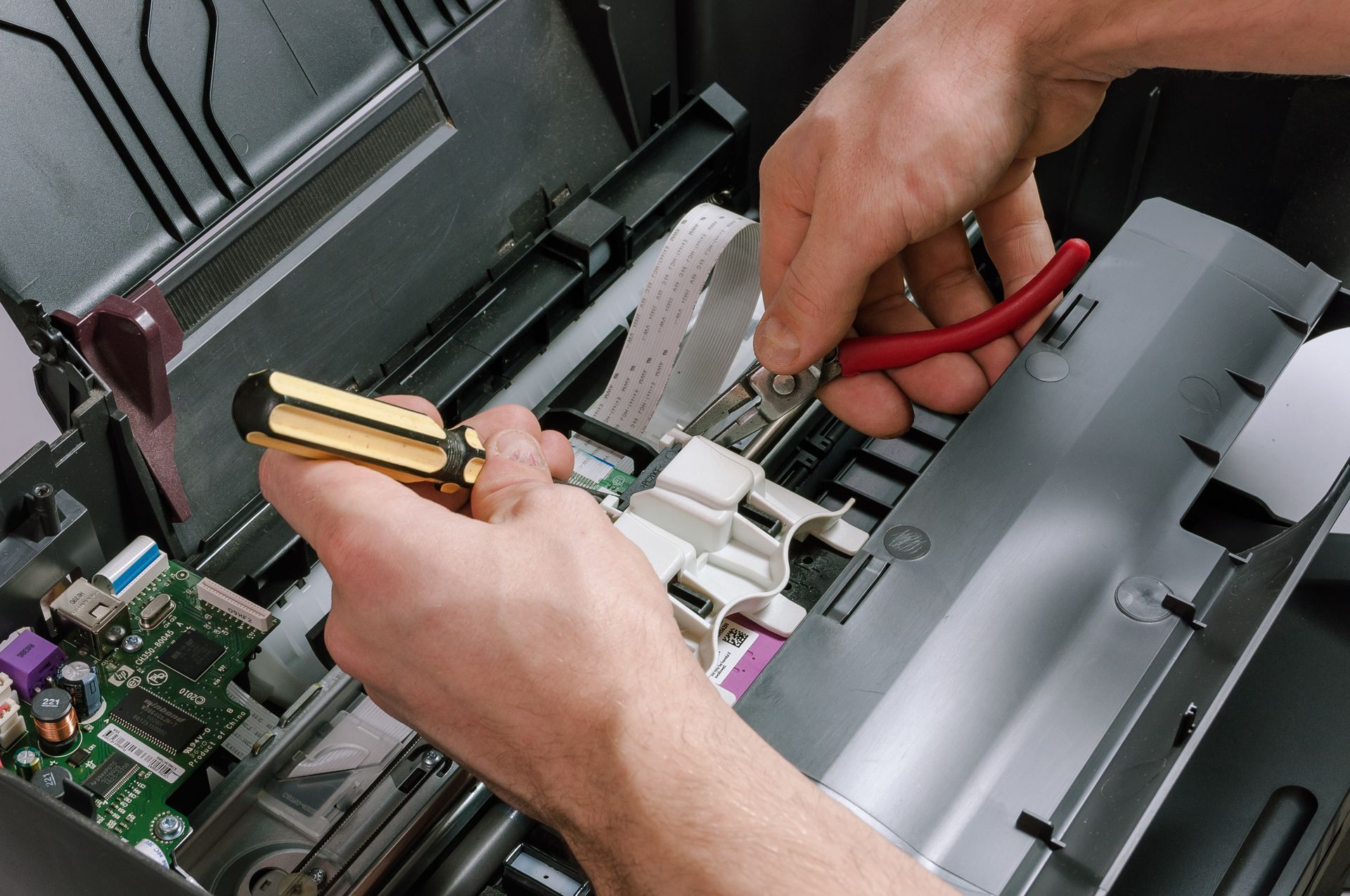 Hands repairing a printer with a screwdriver and pliers.