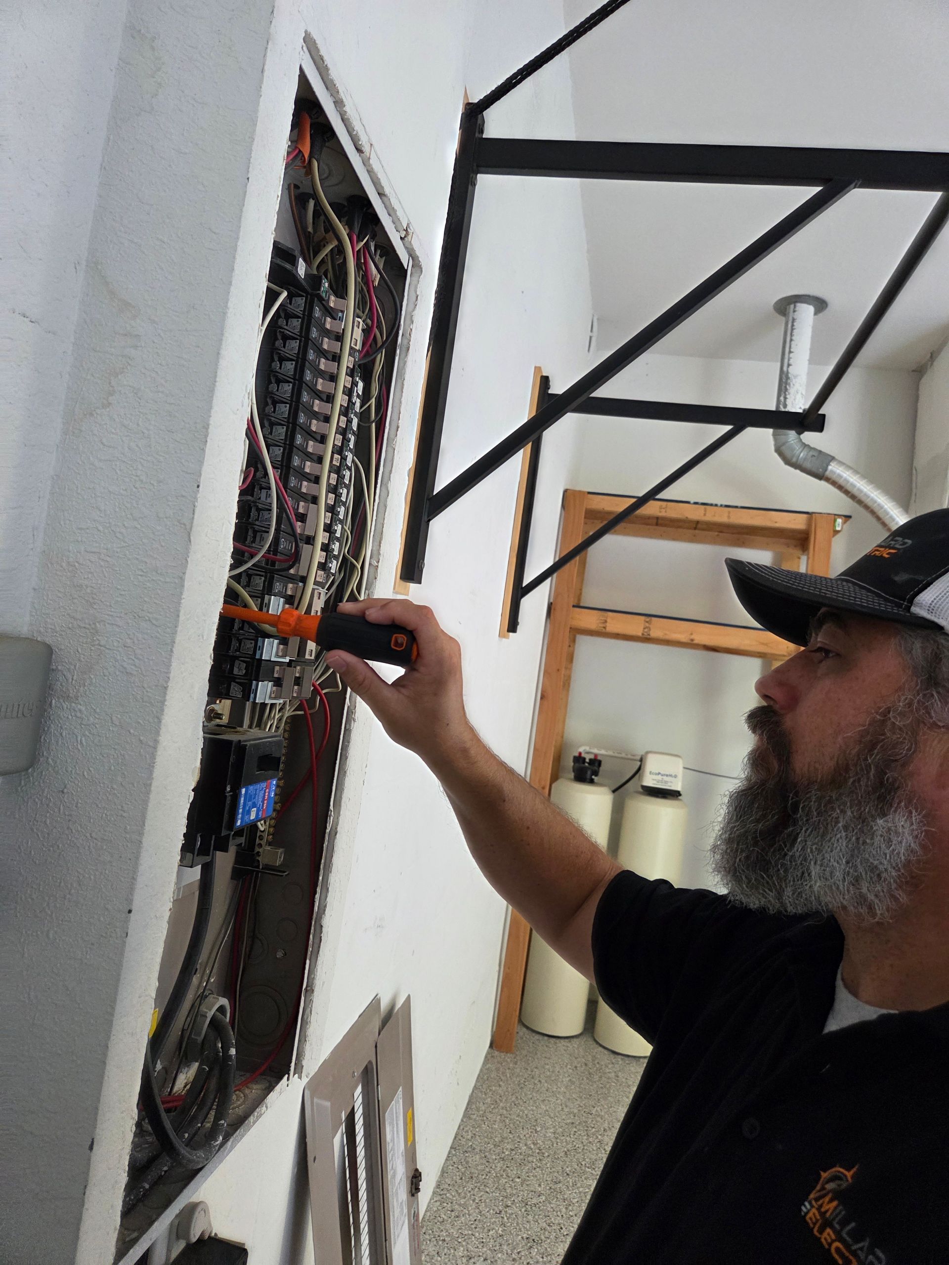A plumber using a wrench on a metal pipe with a white wall background.