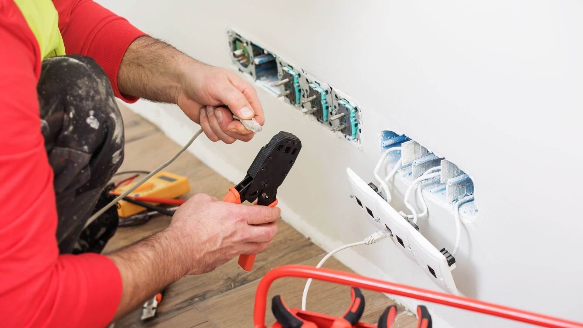 A plumber using a wrench on a metal pipe with a white wall background.