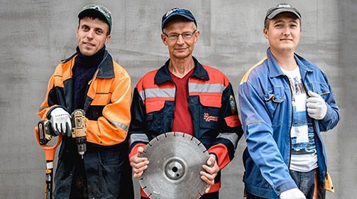 Three construction workers are standing next to each other holding tools.