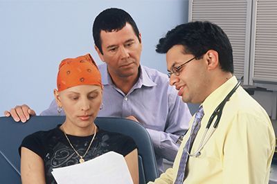 A woman with cancer is sitting in a chair talking to a doctor.