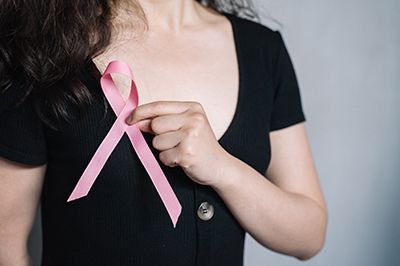 A woman is holding a pink ribbon on her chest.