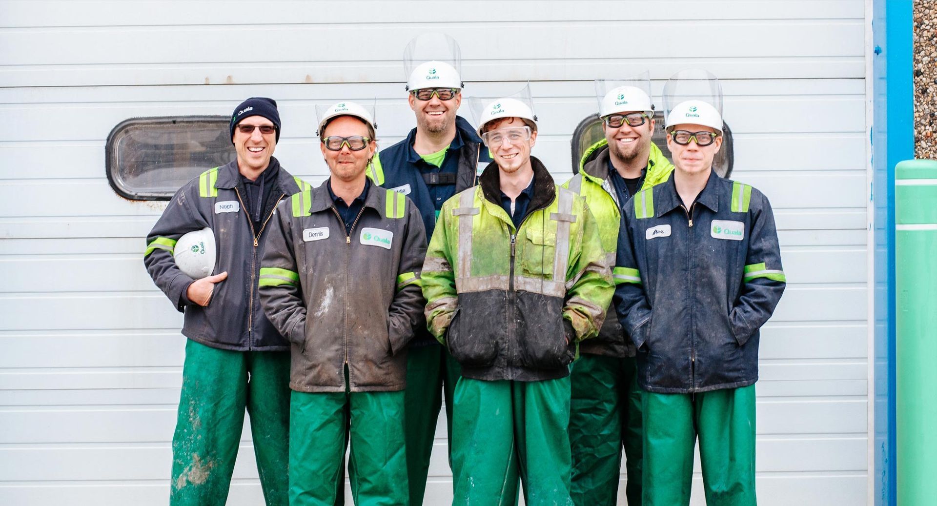 A group of construction workers are posing for a picture in front of a garage door.