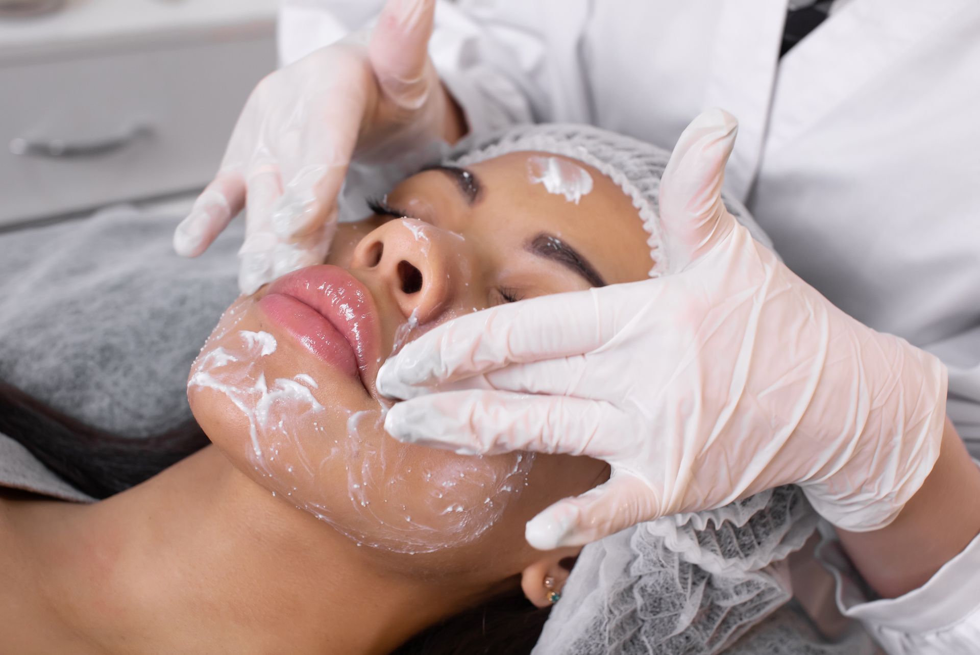Facial treatment: A person's face covered in cream, receiving a massage from gloved hands.
