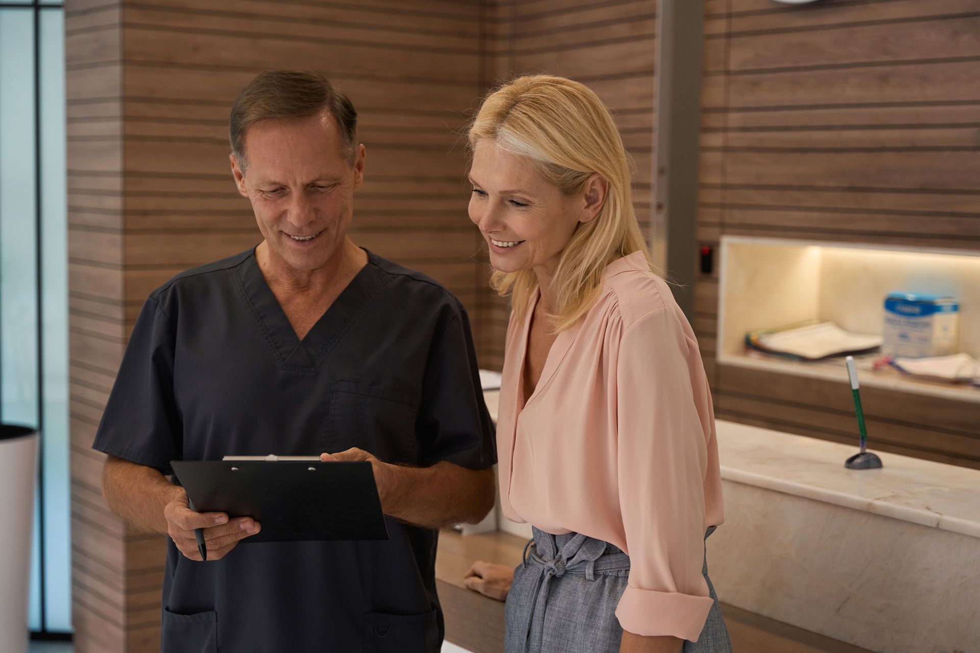 A healthcare provider shows a patient a chart near a reception desk.