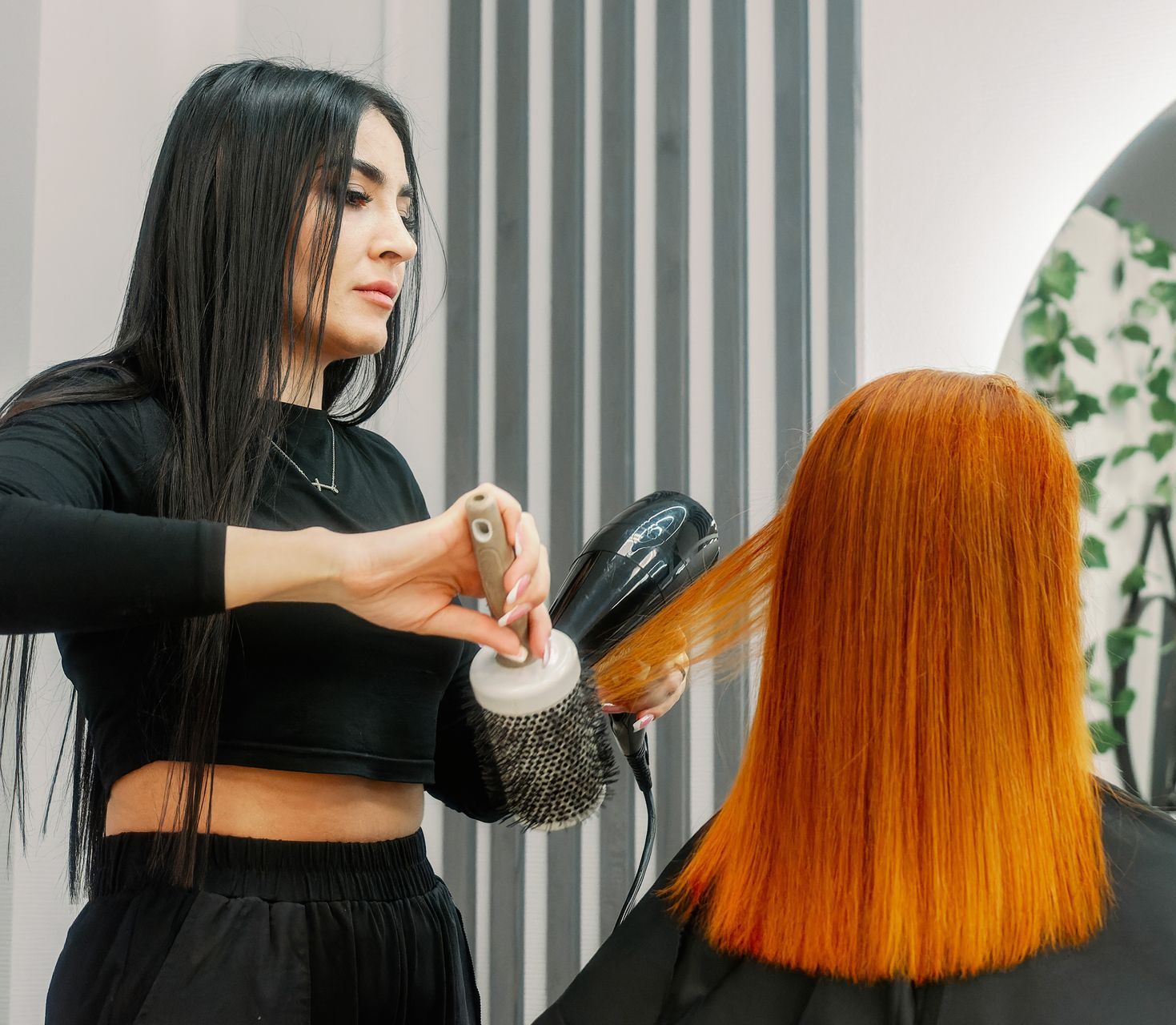 Hair stylist blow-drying client's orange hair with a round brush in a salon.