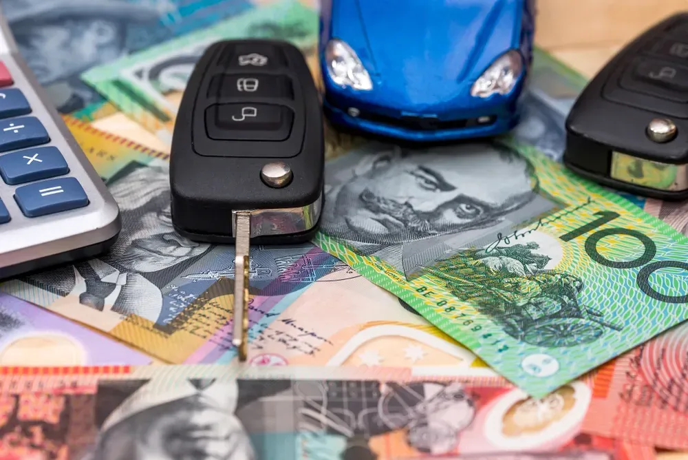 A blue toy car and car keys rest on a pile of Australian currency next to a calculator. — Murwillumbah Motor Wreckers in South Murwillumbah, NSW
