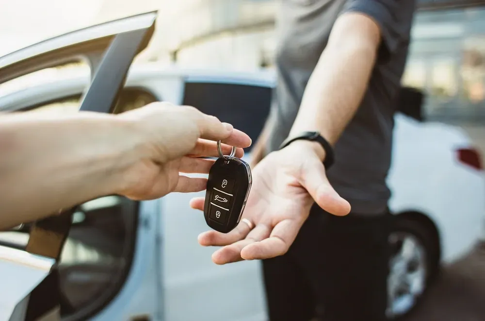 A hand hands a modern black car key fob to another person in front of a white car with an open door. — Murwillumbah Motor Wreckers in Tweed Heads, NSW