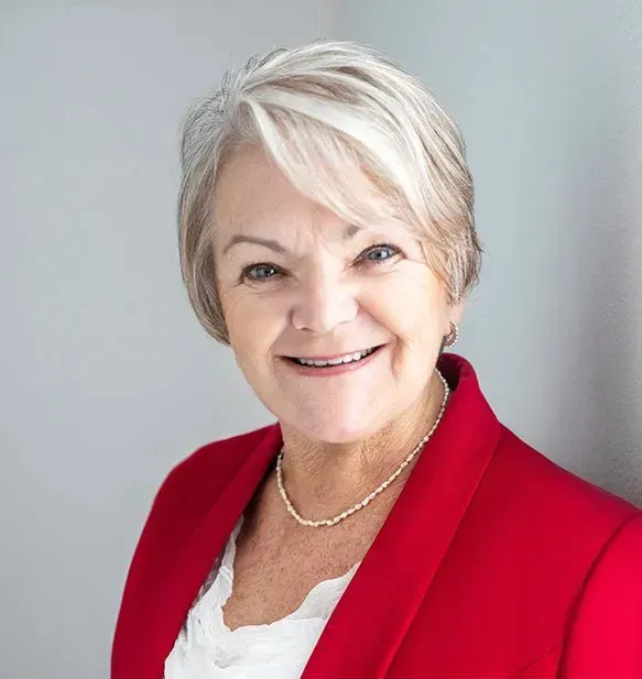 A woman wearing a red jacket and a necklace is smiling for the camera.