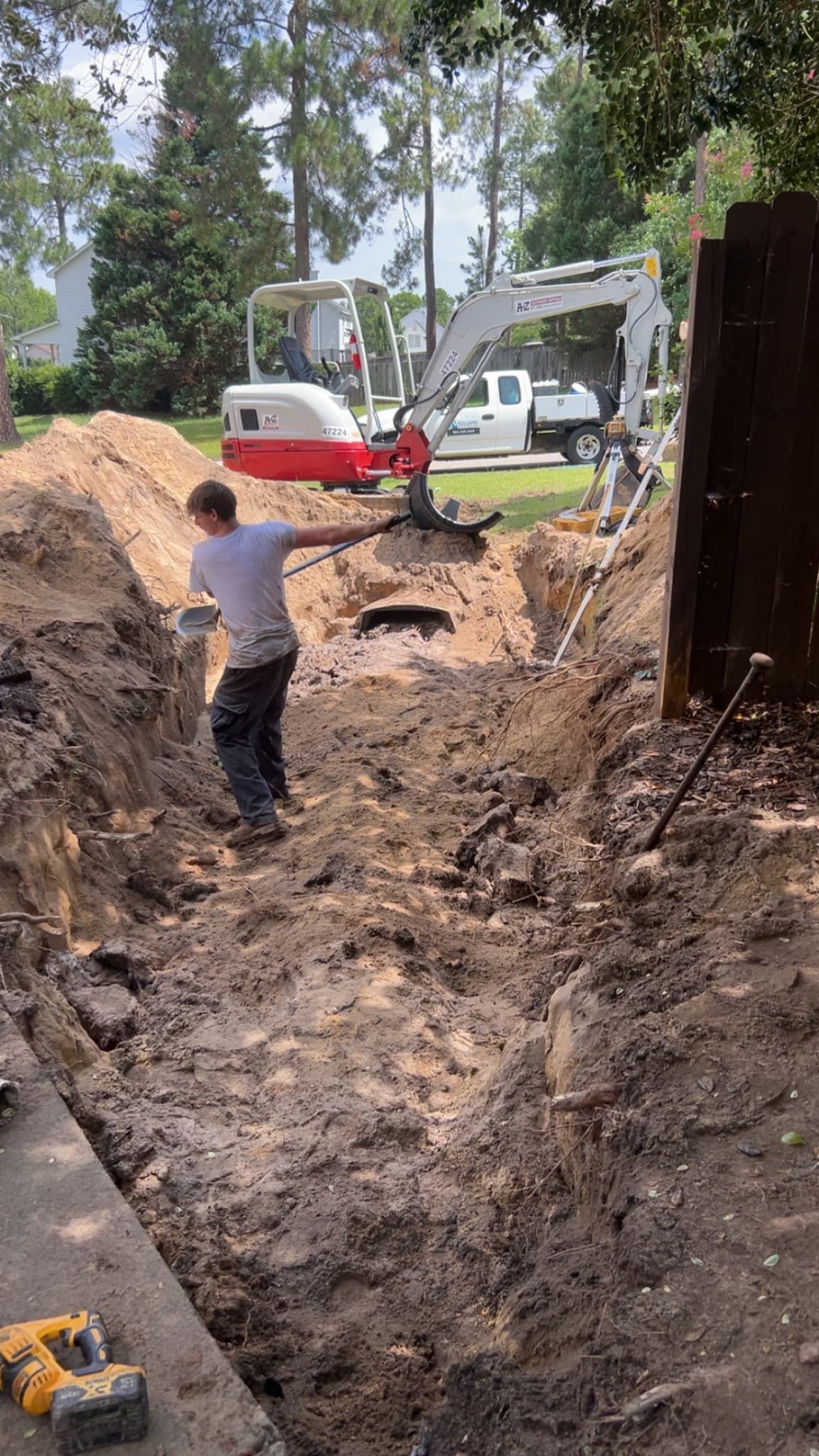 Worker standing in a muddy trench beside an excavator at a construction site