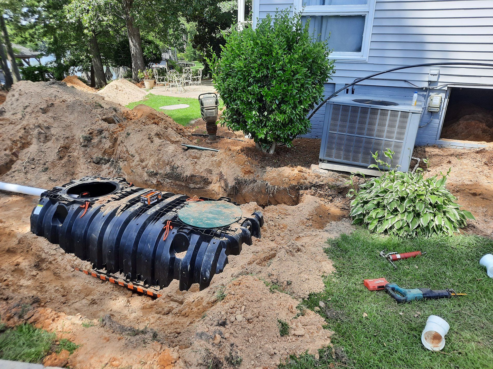 Backyard excavation with black septic tank installed beside a house and dug-up soil around it