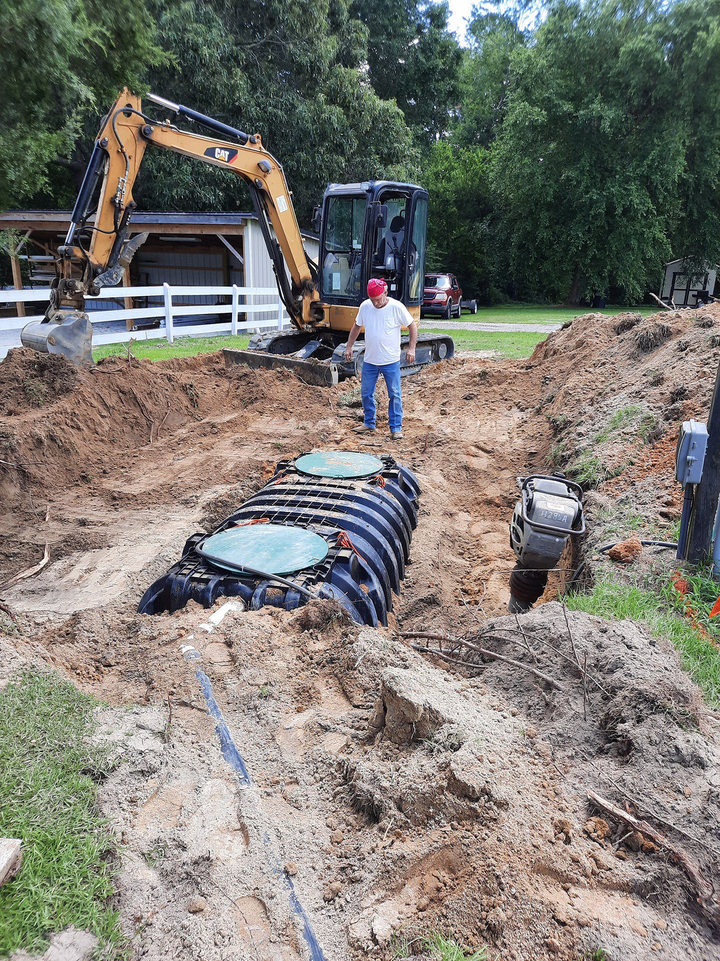 Excavator and worker at a muddy construction site with a large buried pipe chamber.