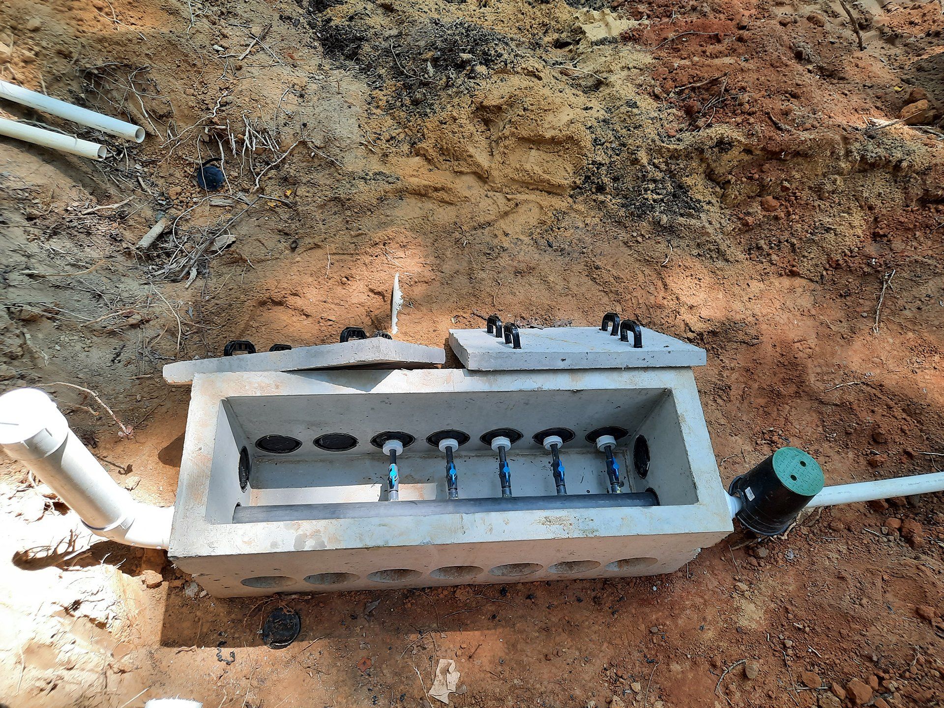 Utility box installed in a dirt trench with exposed white pipes and blue valve on the right