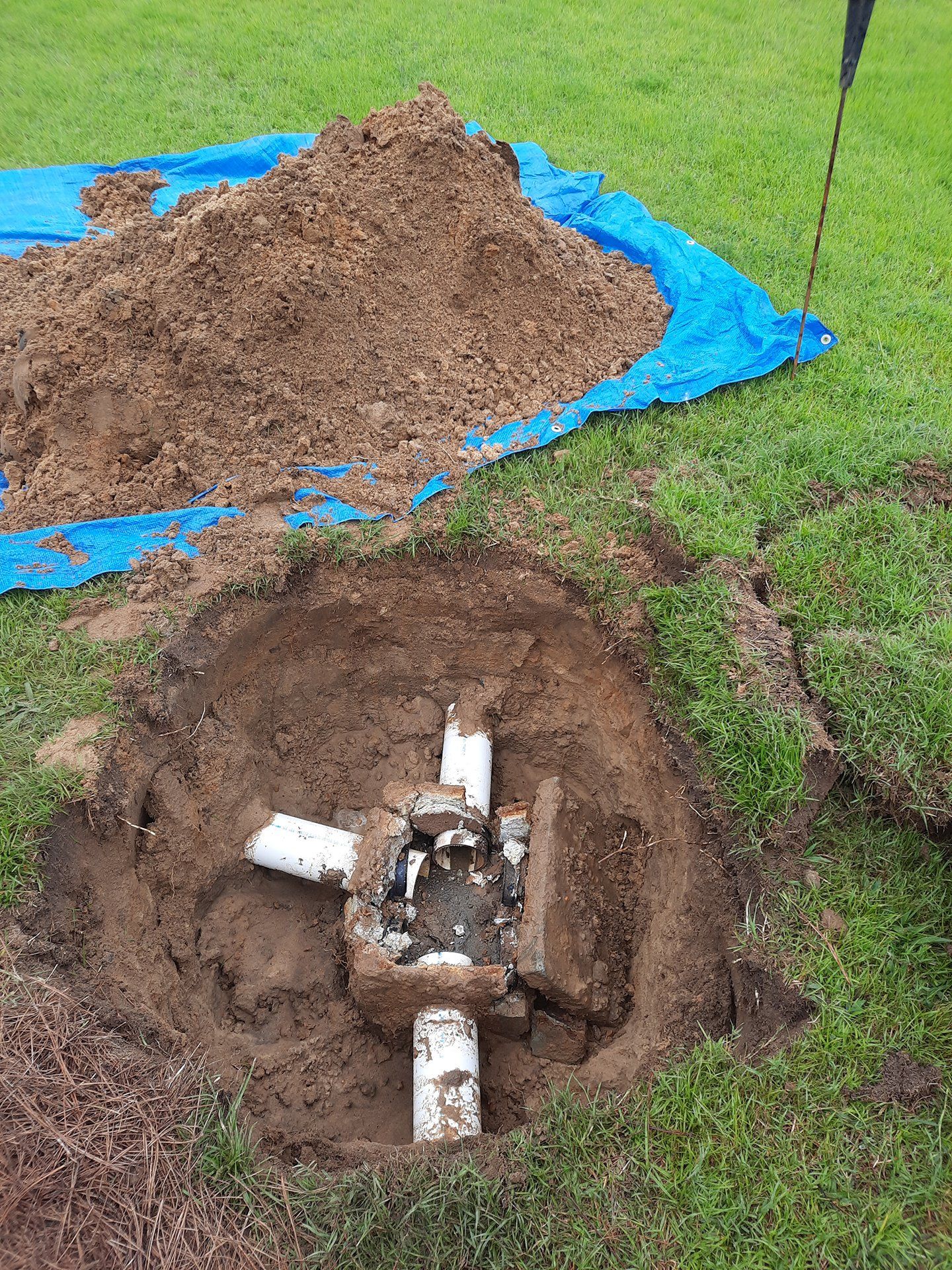 An open ground pipe joint in dirt, with a blue tarp and pile of soil beside it.