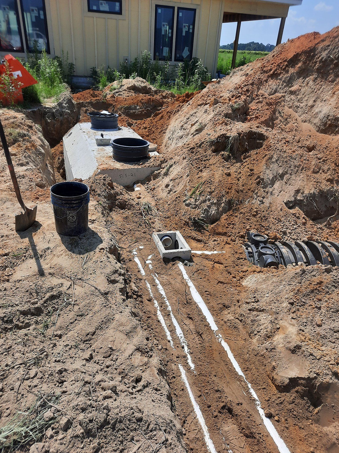 Trenches with white pipes and black buckets at a house under construction beside soil piles