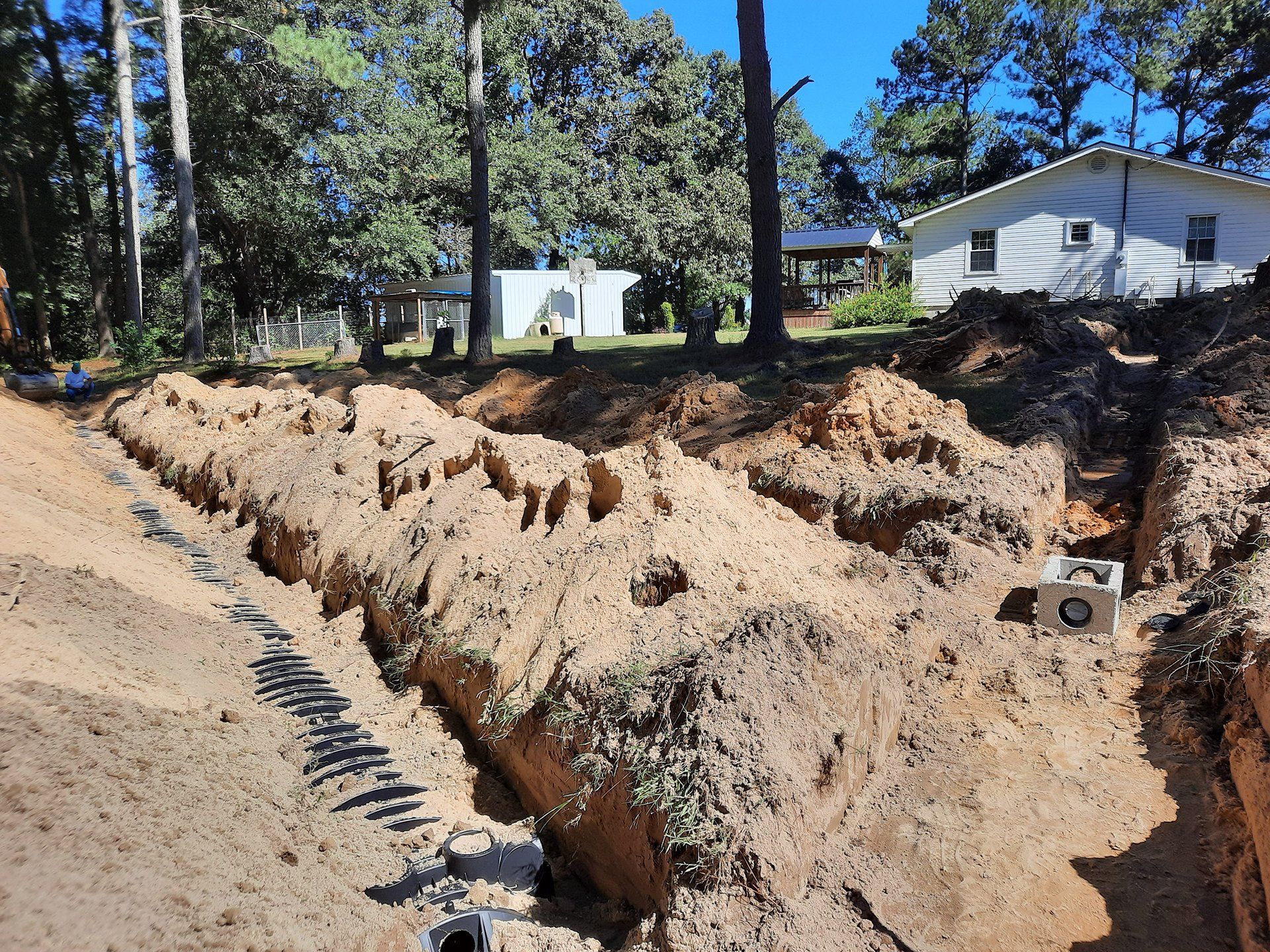 Large dirt trench in a wooded yard with houses in the background