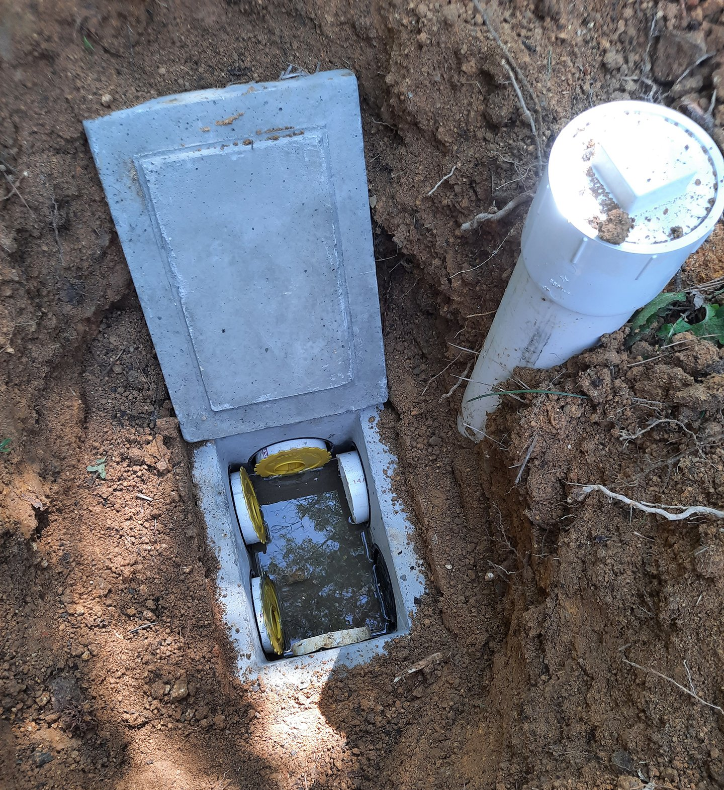 Open electrical or utility box in dirt beside a white PVC pipe