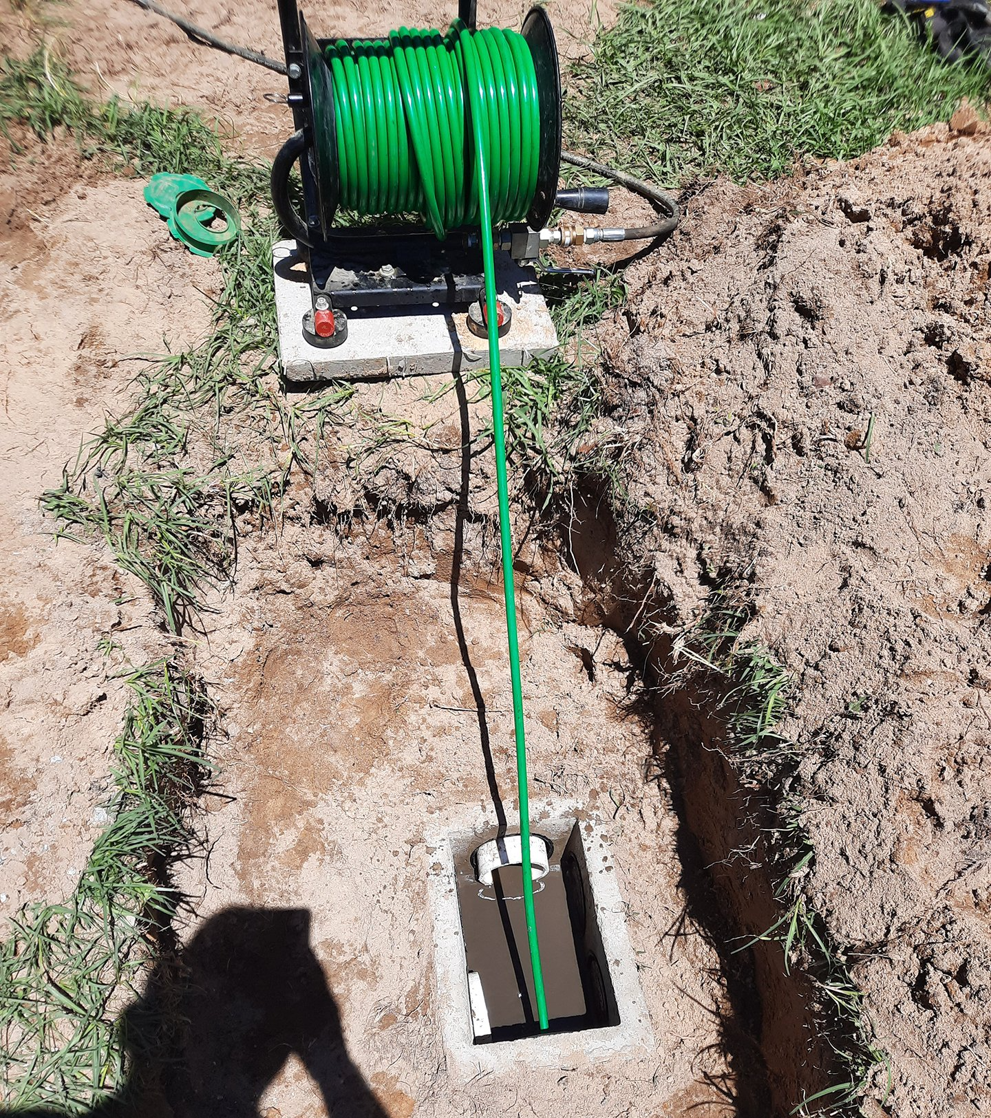 Green cable reel feeding a green cable into a narrow trench in a dug-up yard