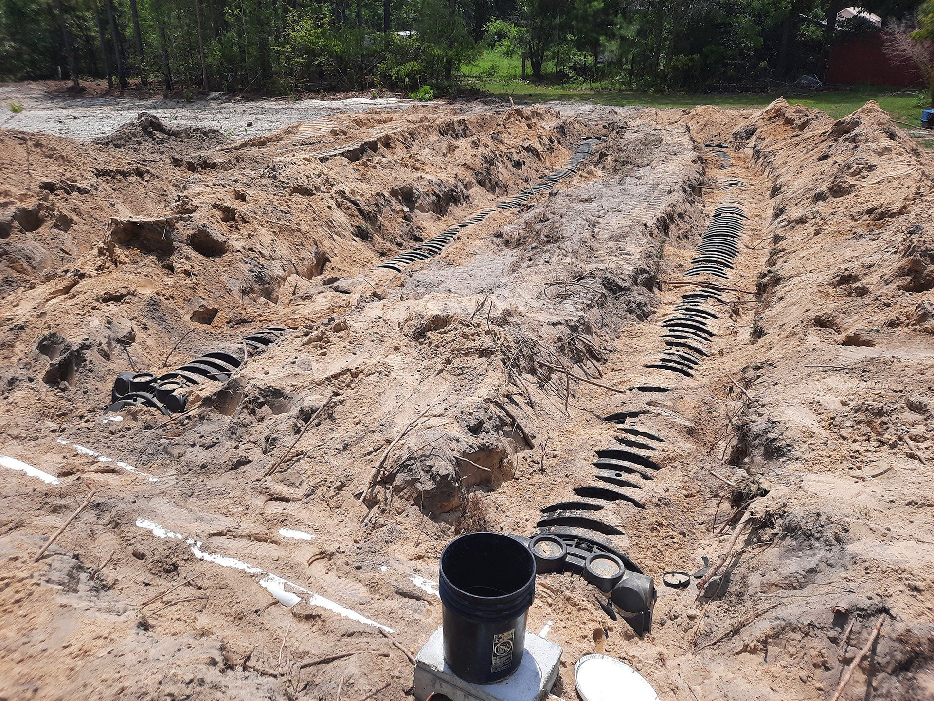 Construction trench with black pipes laid in sandy soil near a wooded area