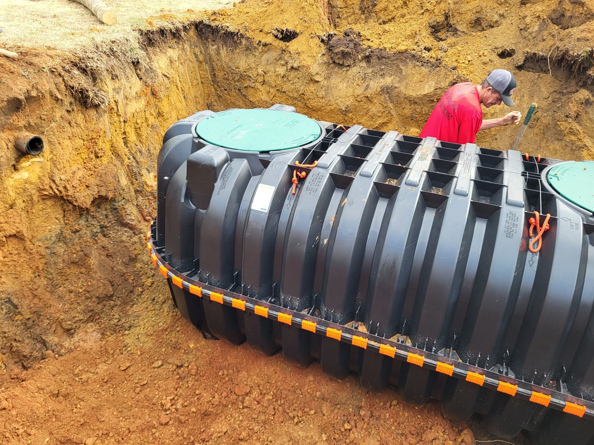 Workers installing a large black cylindrical tank in a dirt excavation pit