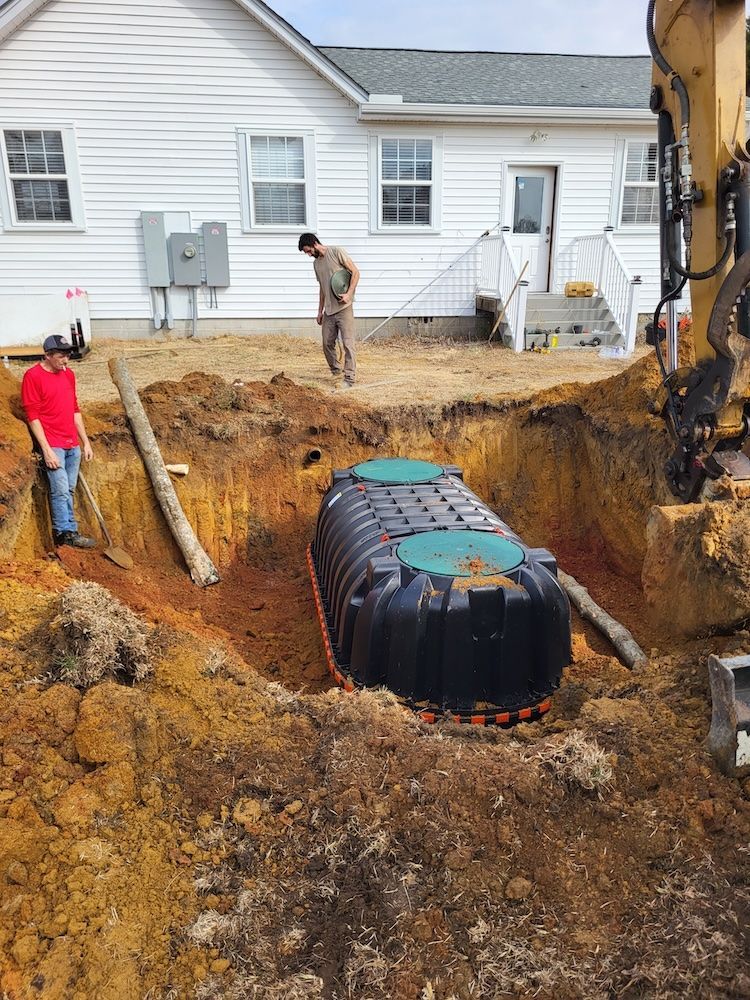 Workers inspect a large dug-out excavation with a black tank beside a house.