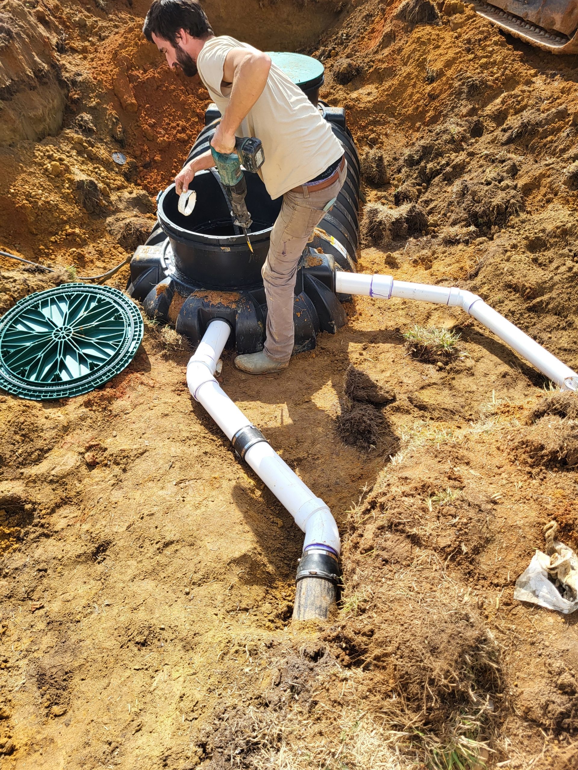 Worker installing black tank and white pipes in a dug-out dirt trench