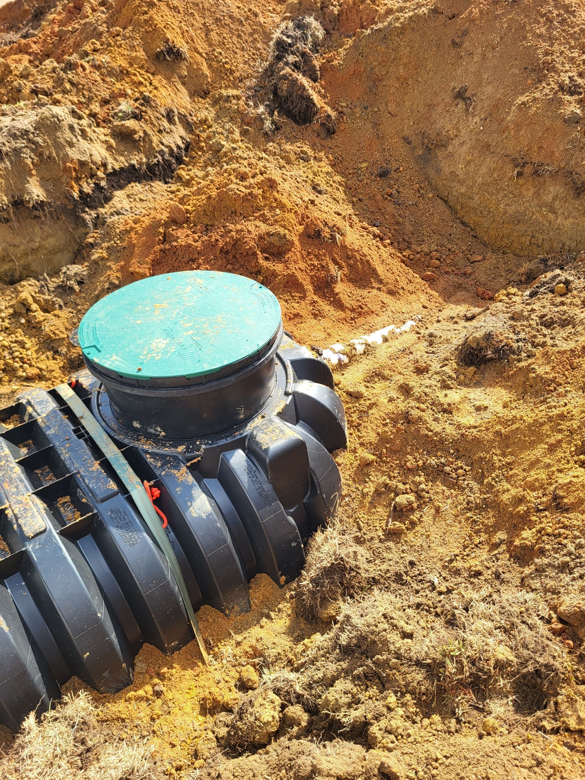 Black pipe fitting with a blue cap in a dirt trench