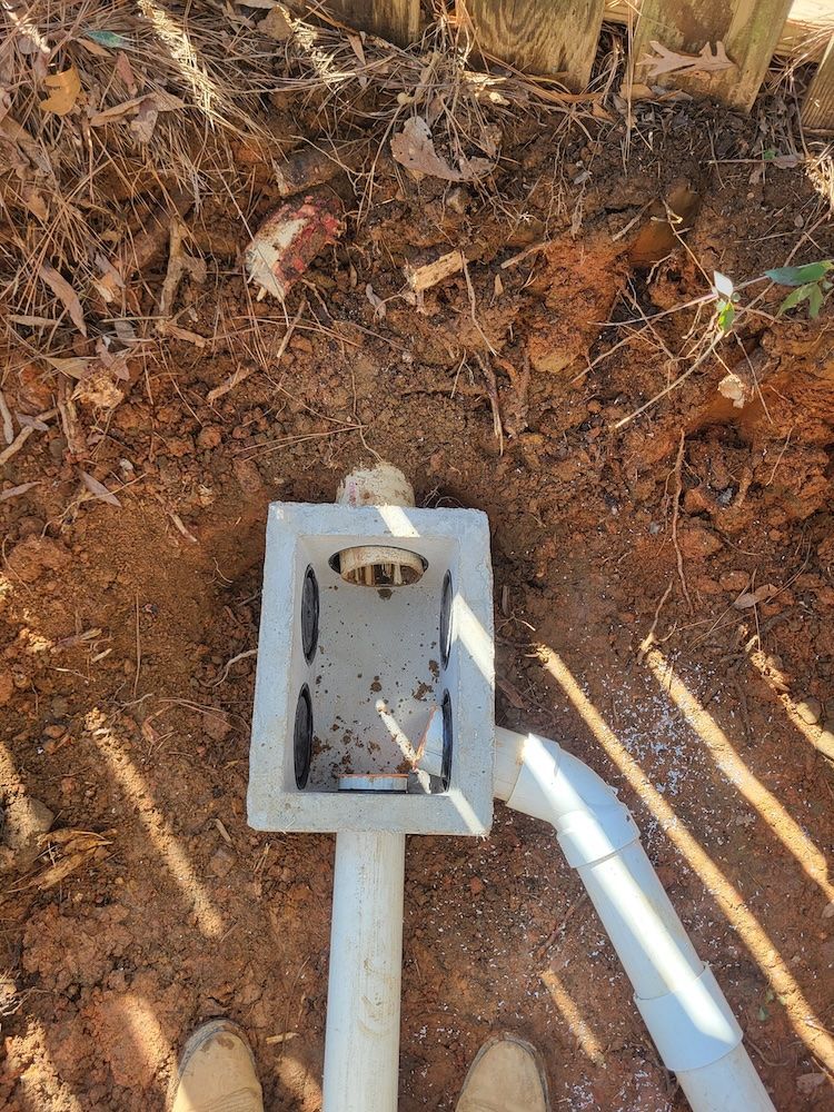 White utility box and conduit pipes in dirt beside a wall, with exposed wiring.