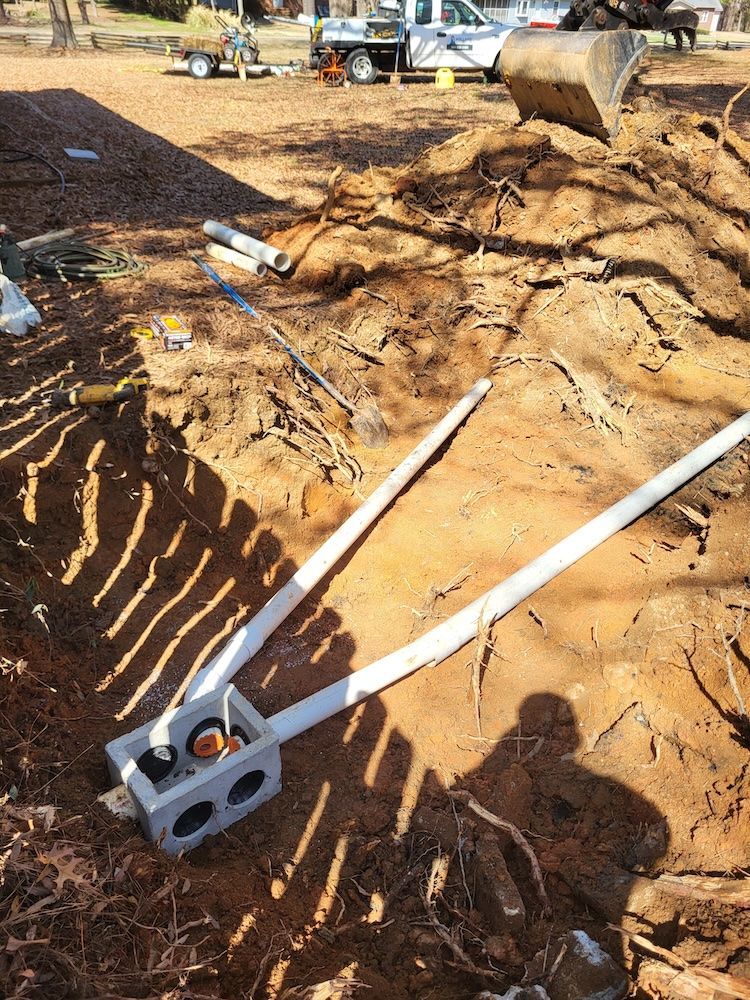 Construction site trench with two long white pipes and a cinder block on sandy ground