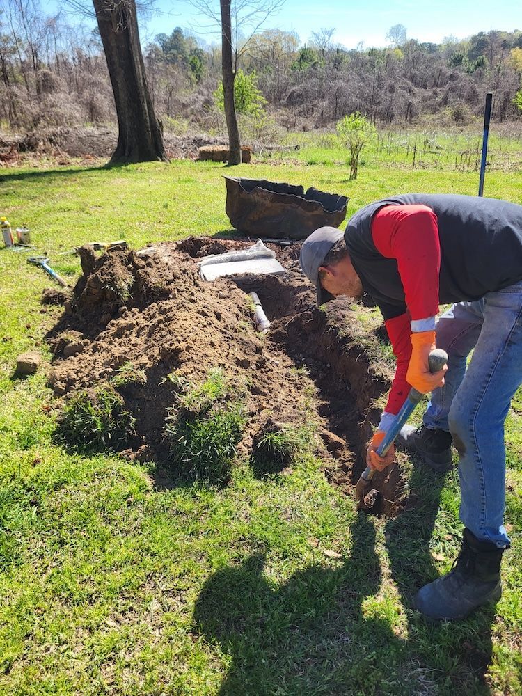 Person in a red shirt digging soil beside a large mound in a sunny grassy field