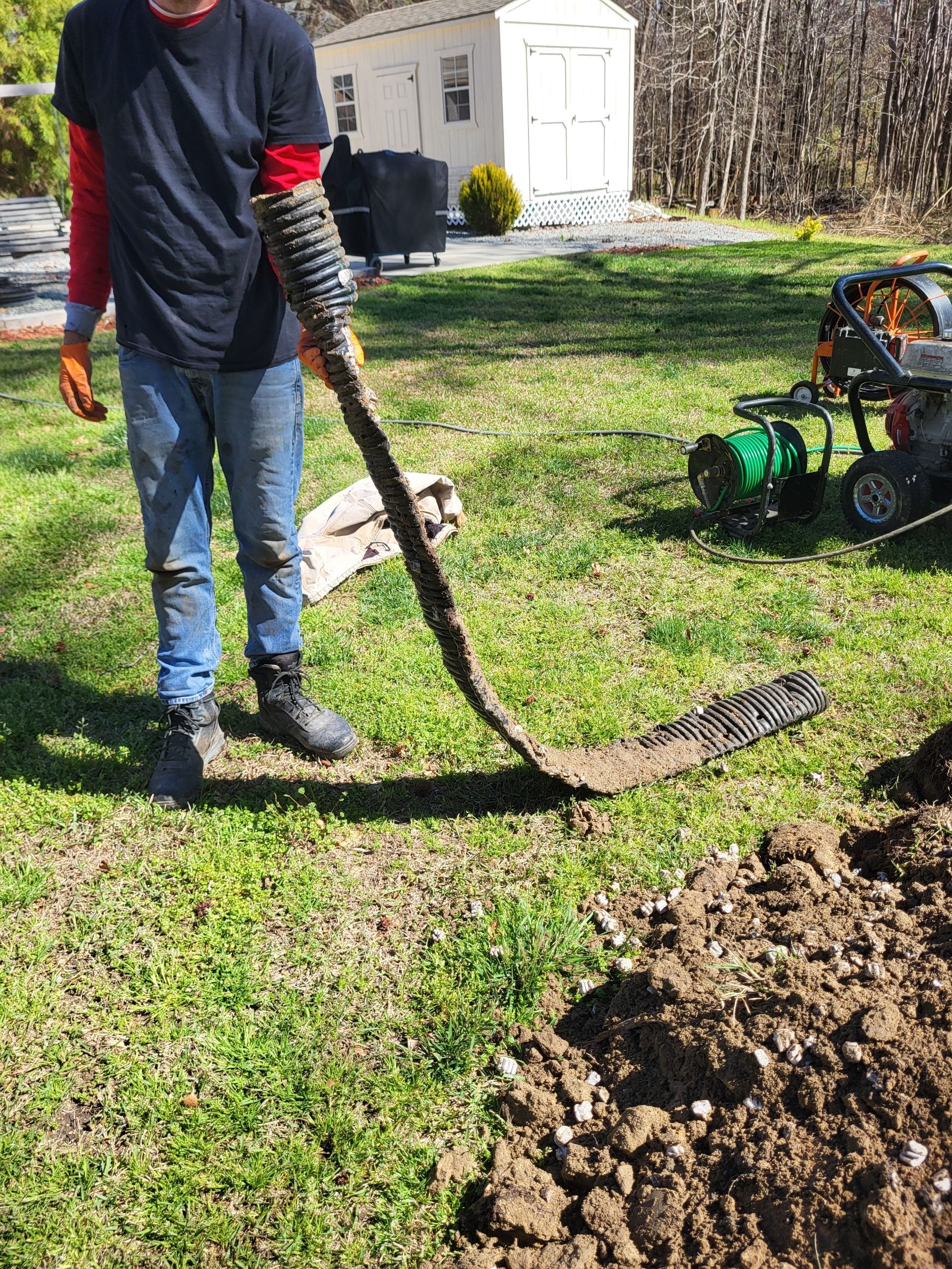 Person using a long tool to dig a trench in a yard near a green utility machine