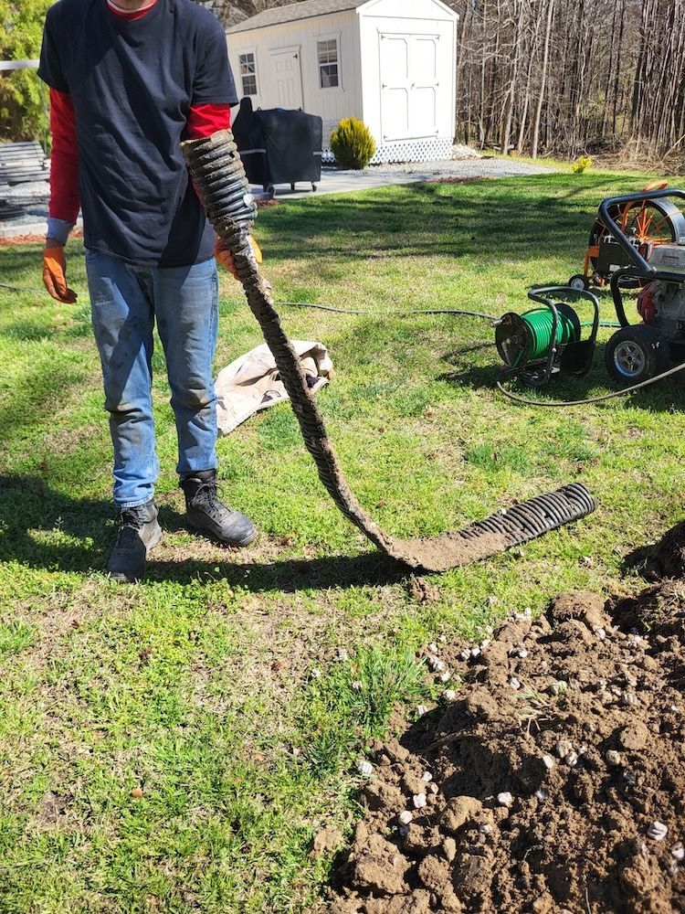 Person using a long-handled rake to clear soil in a yard beside a green machine and dirt pile