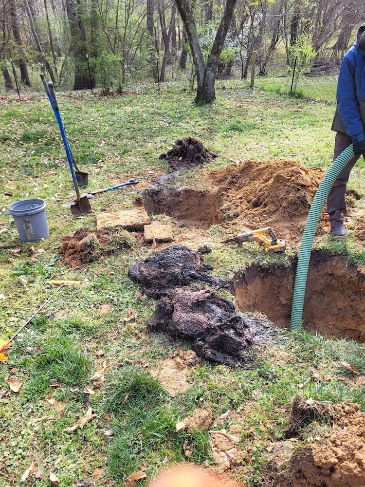 Outdoor trench digging with shovel, hose, and piles of soil in a wooded yard