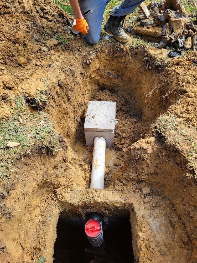Workers digging a trench around a white utility box and pipe in a muddy yard