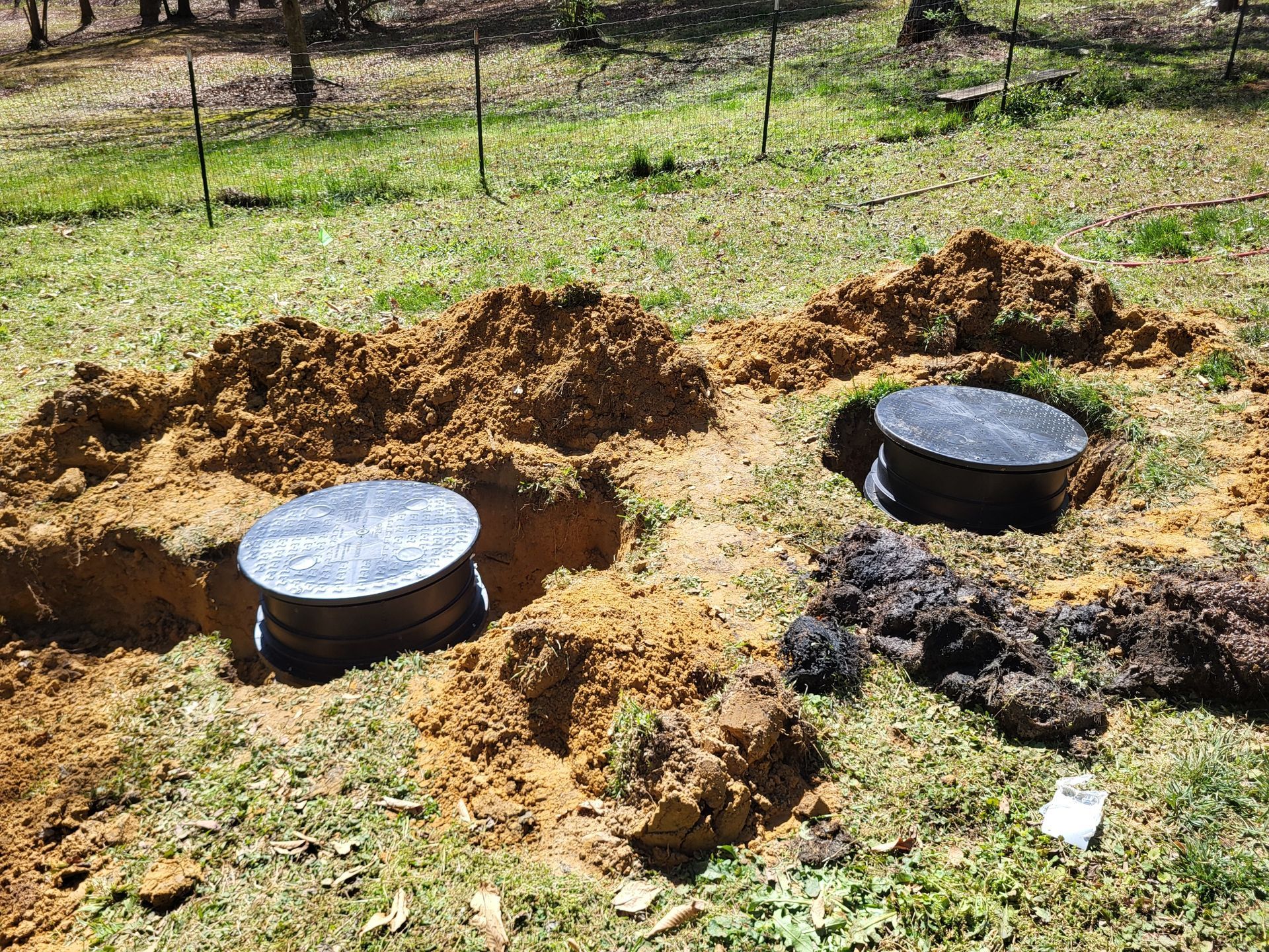 Two round metal containers set in freshly dug dirt in a grassy yard
