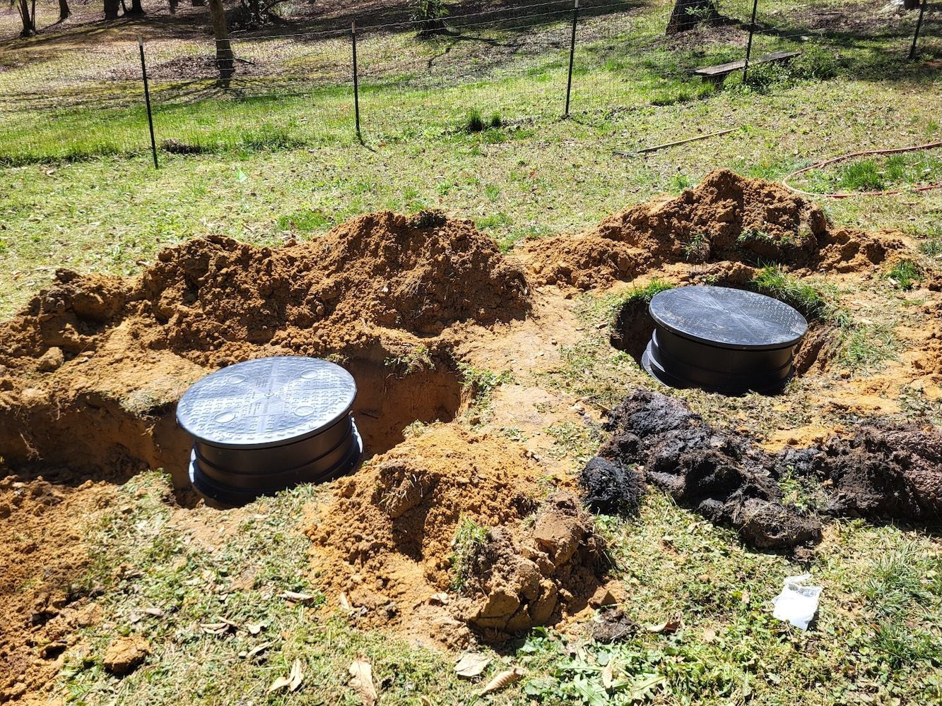 Two round metal lids in a grassy yard beside freshly dug trenches and soil mounds