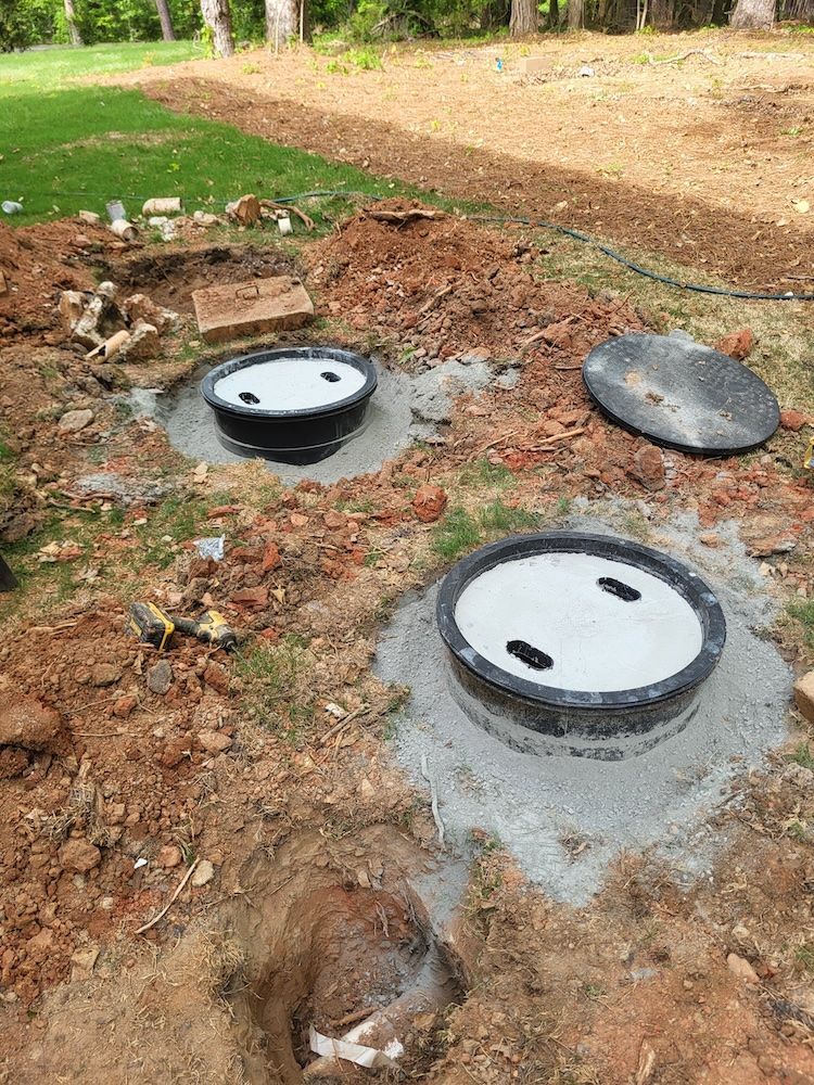 Three round utility access covers in a dirt yard near grass and trees.