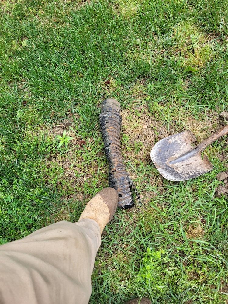 A person’s boot next to a shovel and a charred, blackened object on grass
