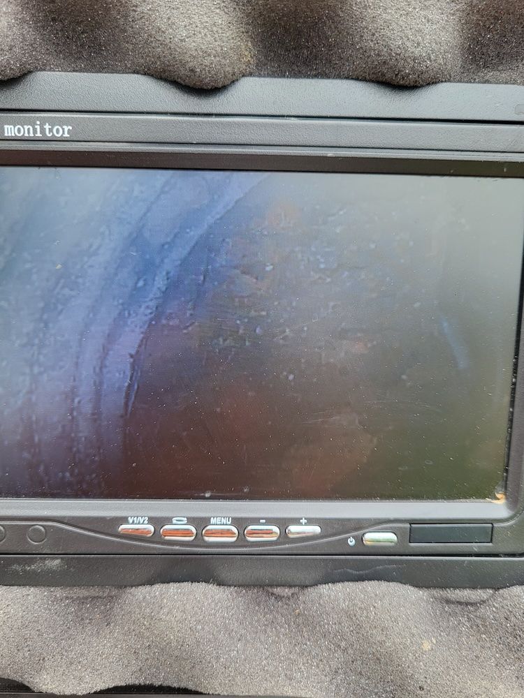 Black monitor screen with a row of buttons, lying on a gray foam surface