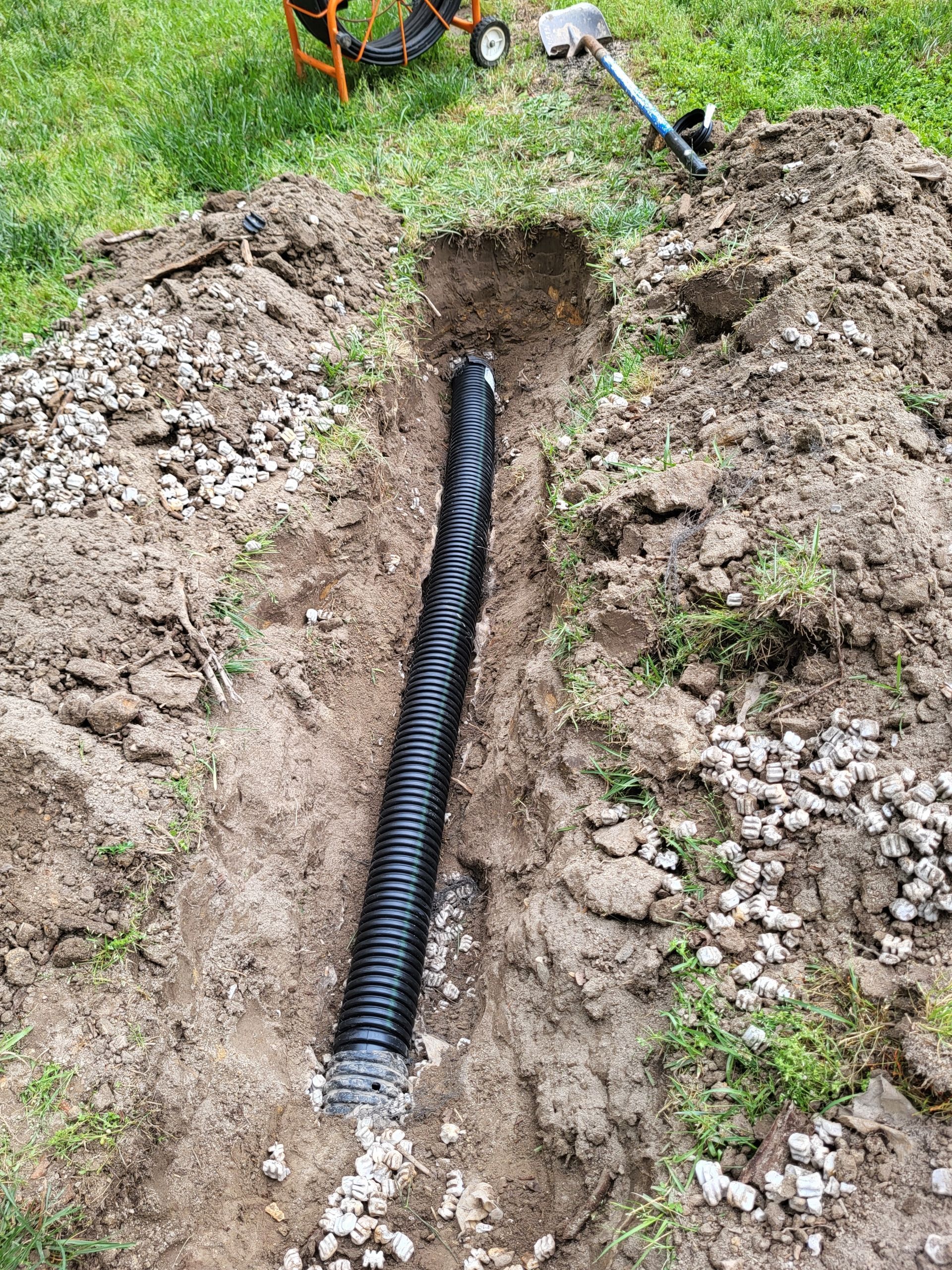 Black corrugated pipe laid in a muddy trench in a grassy yard