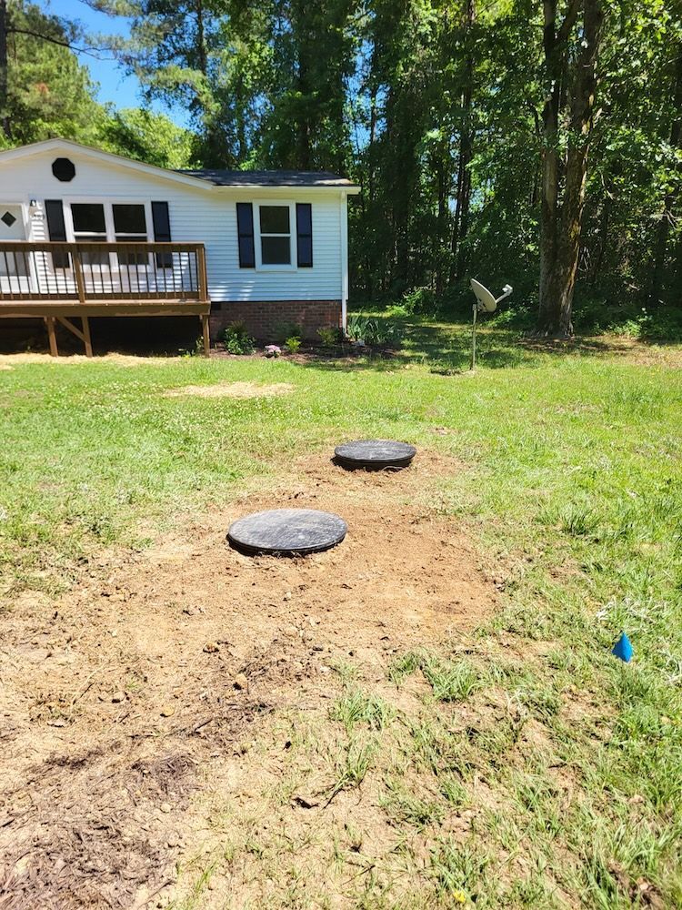 Backyard with a white house deck and two black circular covers in a patchy grassy yard