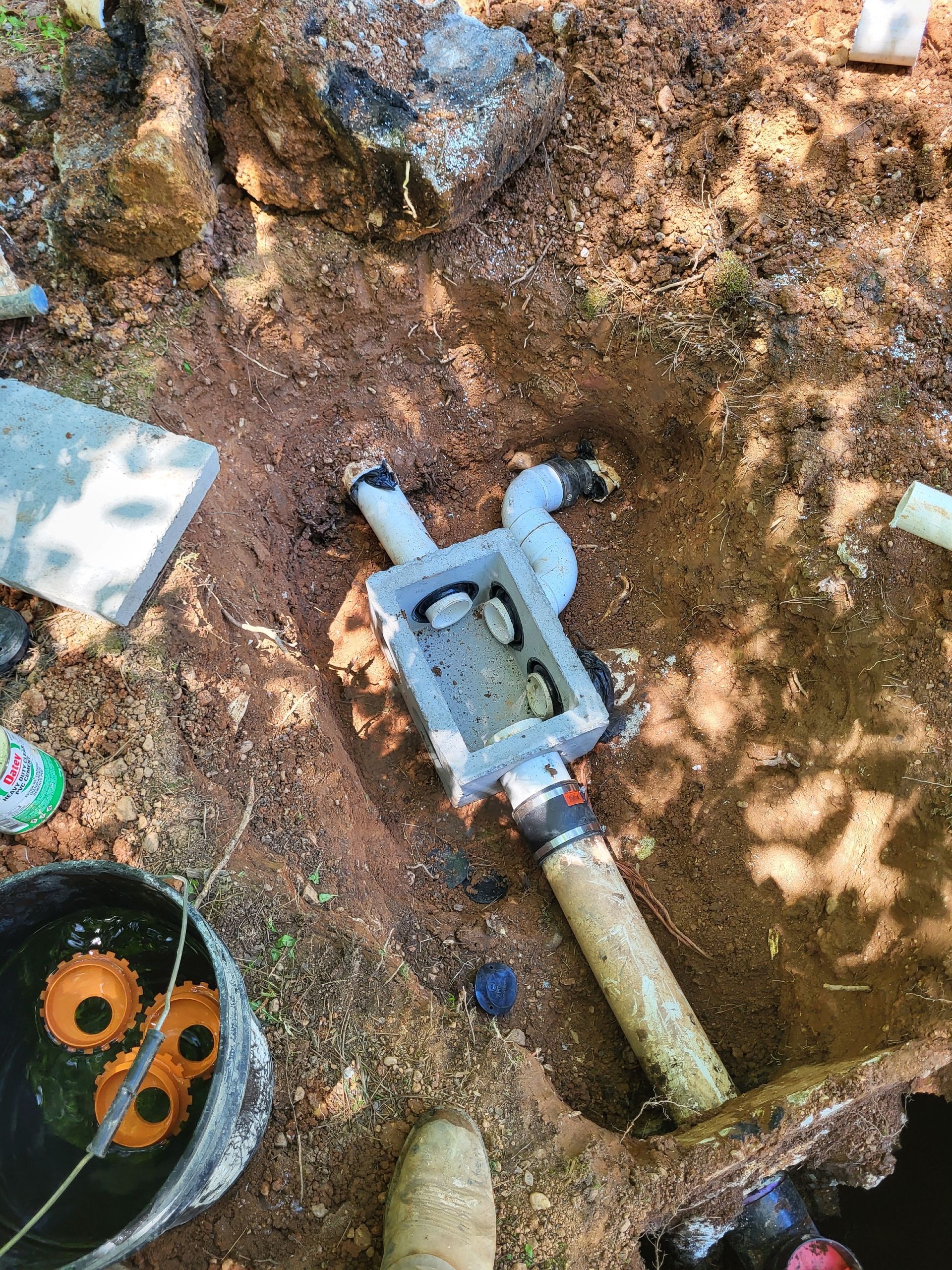 Shallow trench with a blue-gray pipe valve and fittings in dirt, viewed from above.