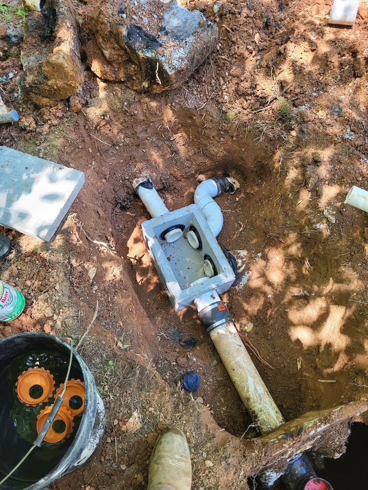 Outdoor utility trench with exposed PVC pipe and gray valve box in muddy soil.