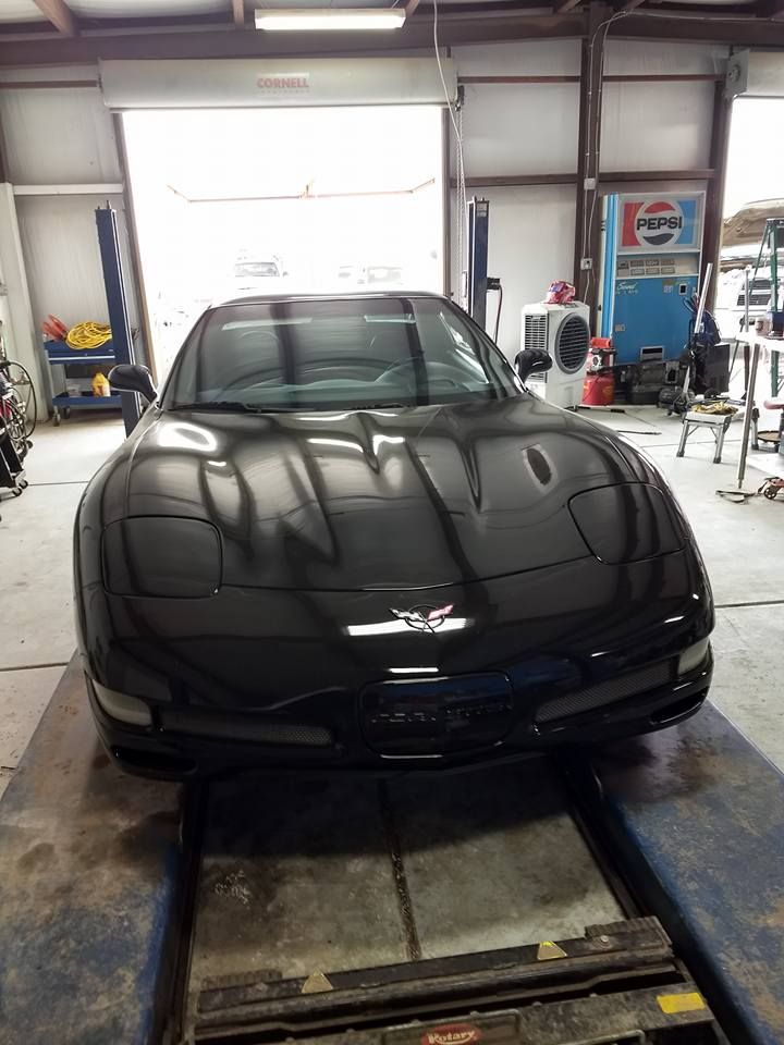 A black Chevrolet Corvette C5 parked inside an automotive repair shop on a car lift.