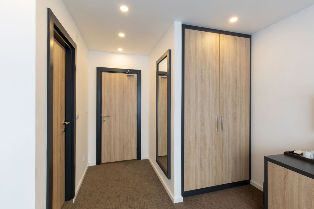 Modern hallway with light wood doors, white walls, brown carpet, and recessed ceiling lights.