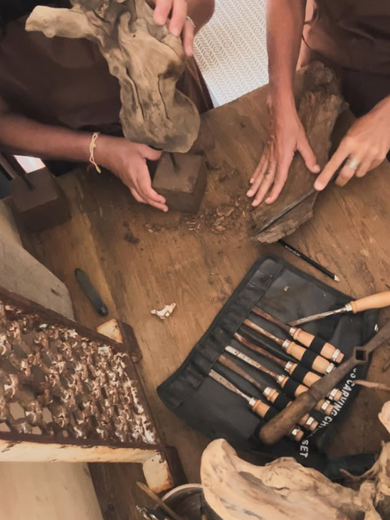 Mani attorno a un banco da lavoro con attrezzi, pezzi di legno e un set di pennelli per un progetto di bricolage.